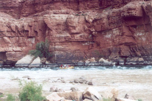 There is a yellow raft doing whitewater rafting close to the center, in the water. Glen Canyon.