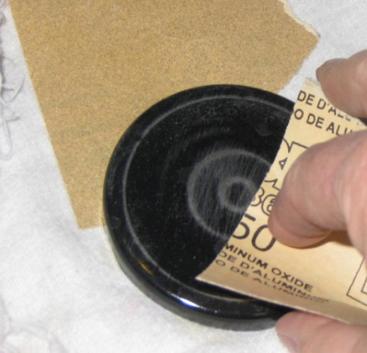 Sand the jar lids. If you're going to paint the entire jar lid, a quick sanding will rough up the surface to let the paint adhere better. Wipe off the dust with a damp rag or paper towel.