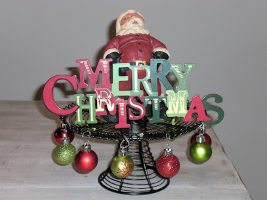 Santa holding a "Merry Christmas" sign on the black wire cake stand.