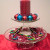 Stacked cake stands with 6" pillar candle surrounded by small ornaments on top and bead garland with candy canes on the bottom layer.