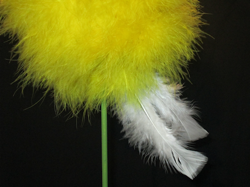 At the base of the yellow ball, right next to the dowel rod, add a feather. Move a little and add another. Keeping working until you have a line of feathers around the middle perimeter of the yellow ball.