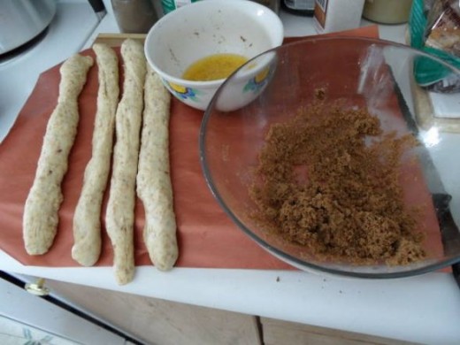 After proofing section the dough into nine and roll them out into thin strips. Dip each strip in melted butter and roll in the sugar mixture. Tie each strip in a simple knot and place in the greased pan. Note the silicon sheet I am working on. It mak